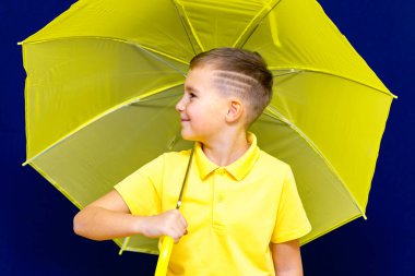 Mavi stüdyo arka planında şemsiyesi olan, beyaz tenli, sarışın, çekici bir çocuk. Çocuk her türlü somurtmayı gösteriyor..