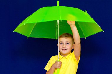 Mavi stüdyo arka planında şemsiyesi olan çekici, oyuncu, beyaz tenli, sarışın bir okul çocuğu. Çocuk her türlü grimi gösteriyor. Görüntüyü kapat.