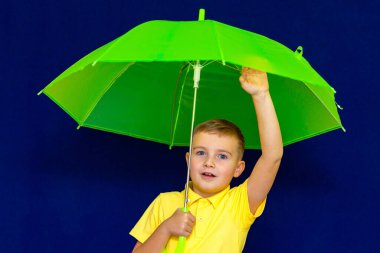 Mavi stüdyo arka planında şemsiyesi olan çekici, oyuncu, beyaz tenli, sarışın bir okul çocuğu. Çocuk her türlü grimi gösteriyor. Görüntüyü kapat.