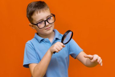 Gözlüklü ve büyüteçten bakan güzel Avrupalı genç bir çocuk. Turuncu stüdyo duvarı..