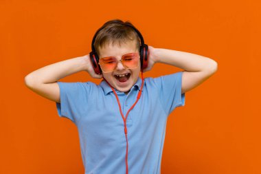 Kırmızı gözlüklü çekici çocuk turuncu stüdyo arka planında kırmızı kulaklıklı müzik dinliyor.