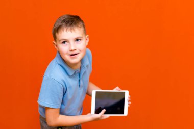 Avrupalı öğrencinin portresi turuncu stüdyo arka planında tablet ve mavi tişört gösteriyor. Neşeli bir şekilde bir şeyler düşünüyor ve boş tablet ekranında bir şeyler gösteriyor. Turuncu zemin. Anlaşıldı, afiş..