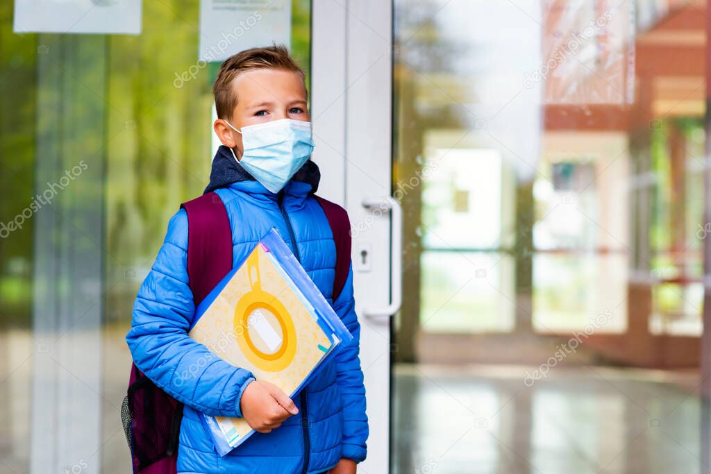 Schoolboy wearing protective mask casual clothes and carry a backpack standing near school. Child going school after pandemic over. students are ready for second pandemic wave