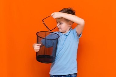 Yan görünüş Mavi tişörtlü okul çocuğu turuncu stüdyo arka planında bardakları çöpe atar