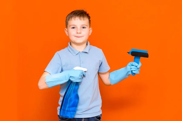 Housekeeping concept. Studio portrait of handsome kid child schoolboy in latex gloves cleaning glass with window dehumidifier sprayer. Orange wall.