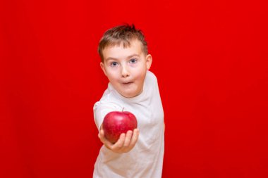 Kapalı Avrupalı çocuk okul çocuğu Apple vitamin, meyve ve sağlıklı yiyecekler veriyor. Parlak kırmızı arka planda mutlu, güzel bir çocuğun önsözü.
