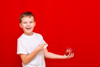 Yandan bakıldığında Avrupalı gülümseyen çocuk okul çocuğu elinde kırmızı bir Elma merhemi tutuyor. Vitaminler, meyveler, sağlıklı yiyecekler. Parlak kırmızı arka planda mutlu, güzel bir çocuğun önsözü.