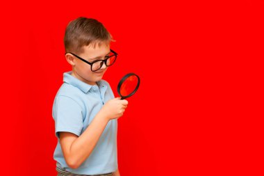 Gözlüklü ve büyüteçten bakan güzel Avrupalı çocuk. Kırmızı stüdyo duvarı..