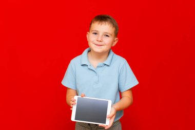 Tabletli bir çocuk. Çocuk biraz düşünceli ve kırmızı arka planda boş tablet gösteriyor.