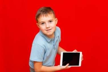 Okul çocuğu öne eğildi ve kırmızı arkaplan reklamında boş tablet gösterdi.