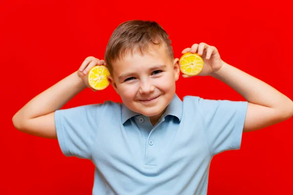 Healthy lifestyle people. Funny smiling image of school boy showing two lemons near the head . Isolated on trendy red background