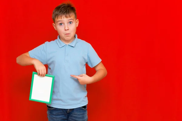 surprised small 9s boy shows a blank board advertisement mock up on red trendy bright background.