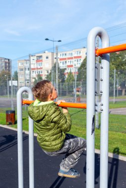 Yan gözle genç çocuk 9 'lu günlük kıyafetleri içinde barfiks çekerek dışarıda egzersiz yapıyor.