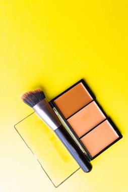 Düz üst görünüm, sarı arka planda gölge fırçası dekoratif kozmetik ürünleri. Uydurma konsept. Metnin için uzay resmini kopyala.