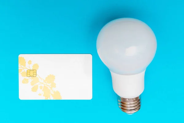 LED lamp and credit card flat lay on blue background. LED bulb. White energy-saving light bulb.Copy space