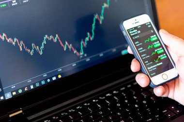 Yatırımcının elleri borsa yatırımlarını finansal gösterge paneli ve akıllı telefon ve bilgisayar ekranlarındaki anahtar performans göstergeleriyle analiz ediyor