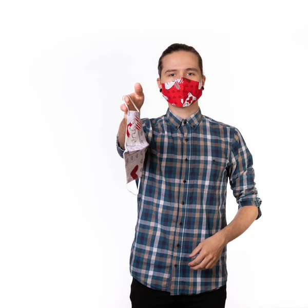 Ekose gömlekli ve kırmızı koronavirüs maskeli beyaz arka planda duran bir adam size bir maske verir.