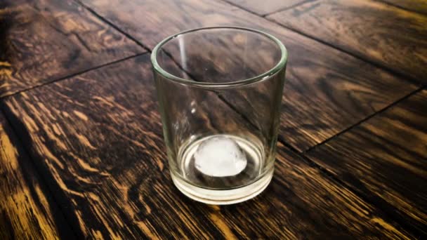 Los cubos de hielo se mueven en un vaso empañado sobre un fondo de mesa — Vídeos de Stock