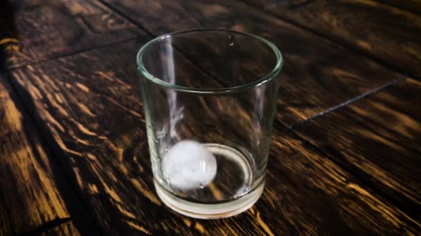 Los cubos de hielo se mueven en un vaso empañado sobre un fondo de mesa — Vídeo de stock