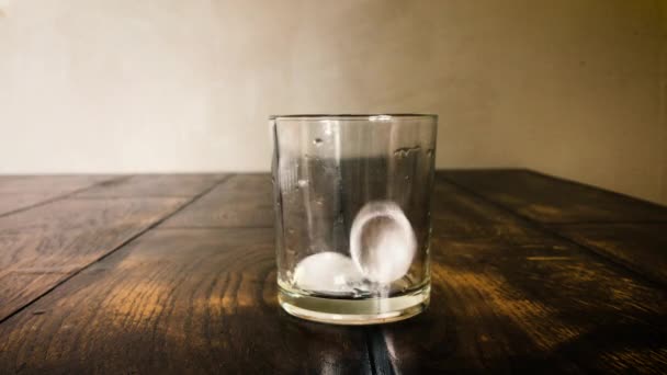 Los cubos de hielo se mueven en un vaso empañado sobre un fondo de mesa — Vídeos de Stock