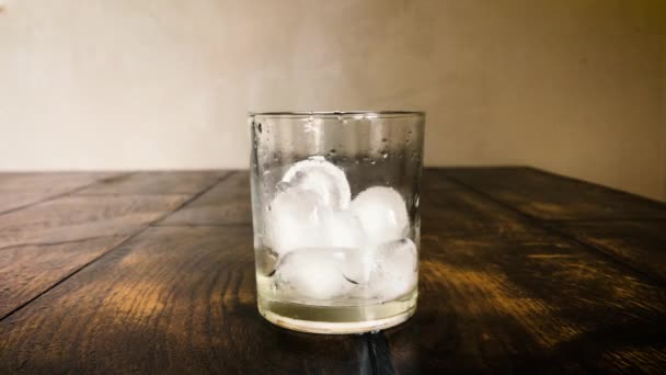 Los cubos de hielo se mueven en un vaso empañado sobre un fondo de mesa — Vídeos de Stock