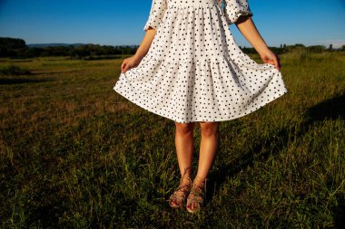Çimlerin üzerinde kadın bacakları. Gün batımında yeşil çimlerin üzerinde açık renk bir elbiseyle genç kız bacakları. Güzel, genç kız güneşli hava. Beyaz elbiseli bir kız. Pedikür ayaklı.