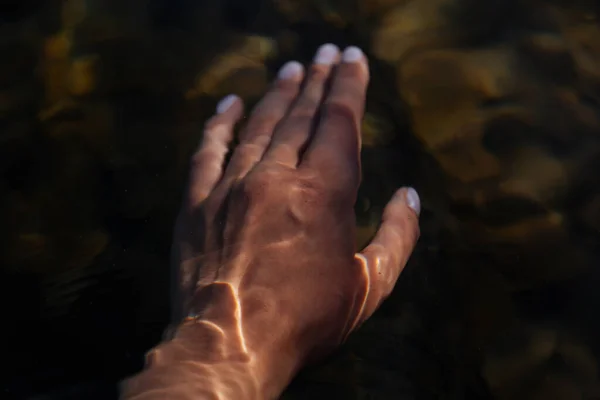 Hand Immersed in water.Shadows on the water. Sun shine in the morning.Young woman\'s hand touching the water in the sea.Hand refreshing in a crystal clear water.