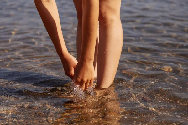 Tropik plajda kumla, vücut parçalarıyla rahatlamış bir kadın. Kadın eli ve ayakları suyun arka planında. Pasifik sahilinin ıslak kumlarında duruyor.