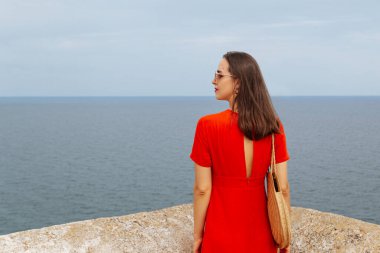 Kırmızı elbiseli ve deniz manzaralı genç bir kadın. Denize bakan yalnız bir genç kız..