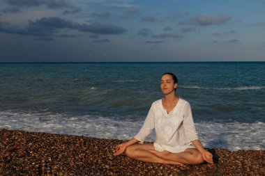 Denizin önünde yoga yapan çekici bir kız. Bir plajda nilüfer pozisyonunda oturan ve yoga yapan genç bir kadın portresi.