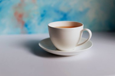 Mavi arkaplanda beyaz çay fincanı ve çay tabağı. Mavi kahve fincanı mavi grunge arkaplanda beyaz masada.