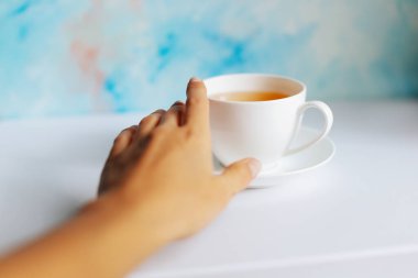 Bir kadın eli beyaz masada bir fincan çay tutar. Beyaz arka planda yeşil çay.