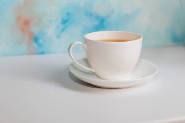 Mavi arkaplanda beyaz çay fincanı ve çay tabağı. Mavi kahve fincanı mavi grunge arkaplanda beyaz masada.