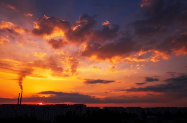 Renkli Sihirli Günbatımı. Gün doğumunda şehir evlerinin çatıları. Kuşlar gökyüzünde uçuyor. Termik santral borusundan siyah duman geliyor..