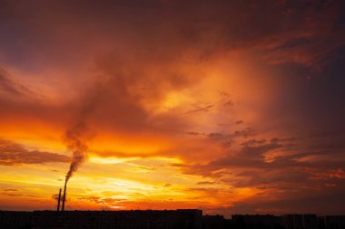 Renkli Sihirli Günbatımı. Gün doğumunda şehir evlerinin çatıları. Kuşlar gökyüzünde uçuyor. Termik santral borusundan siyah duman geliyor..