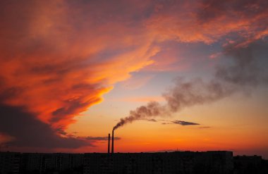 Renkli Sihirli Günbatımı. Gün doğumunda şehir evlerinin çatıları. Kuşlar gökyüzünde uçuyor. Termik santral borusundan siyah duman geliyor..