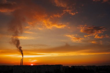Renkli Sihirli Günbatımı. Gün doğumunda şehir evlerinin çatıları. Kuşlar gökyüzünde uçuyor. Termik santral borusundan siyah duman geliyor..