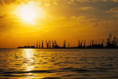 Ateşli günbatımı gökyüzü ve deniz ile güzel bir manzara. Gün doğarken kıyıda liman. Turna siluetleri ateşli, turuncu ve kırmızı gökyüzüne karşı. 