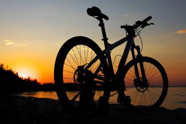 Deniz, altın gökyüzü arka planda renkli günbatımı karşı sahilde Bisiklet silüeti. Su güneşte yansımasıdır. Açık havada