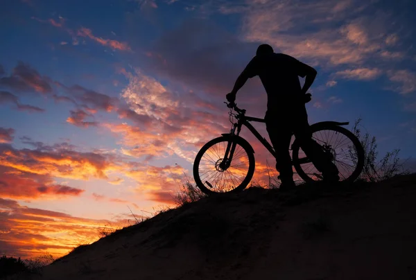 Silhouette of sports person cycling on the meadow on the beautiful sunset. Young man riding bicycle.