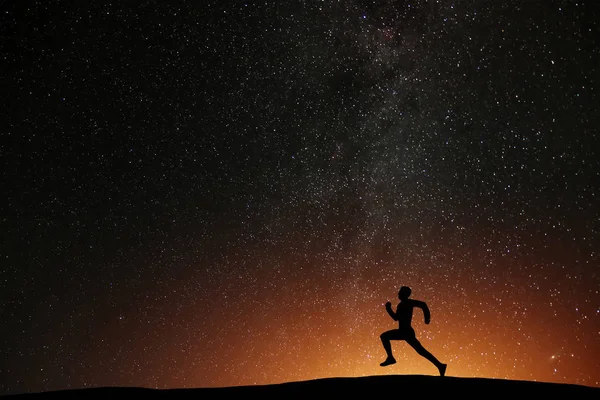 Güzel yıldızlı gece arka plan ile tepe üzerinde çalışan runner atlet. Egzersiz karanlık zaman, sağlık kavramı koşu adam silüeti.