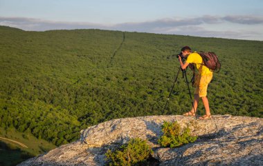 Fotoğrafçı ile tripod ve akşam kayada sırt çantası.