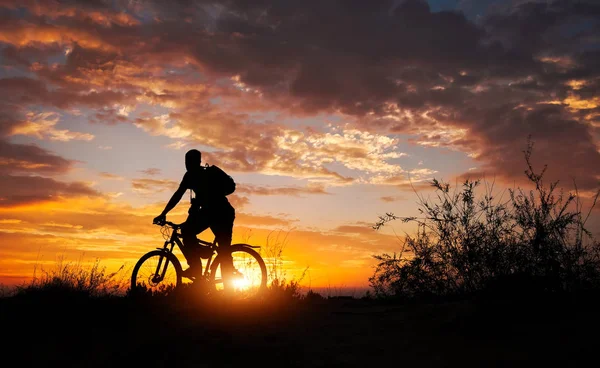 Silhouette of sports person cycling on the meadow on the beautif