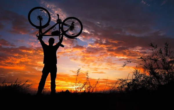 Sylwetka człowiek stanąć w akcji podnoszenia rower nad jego HEA — Zdjęcie stockowe