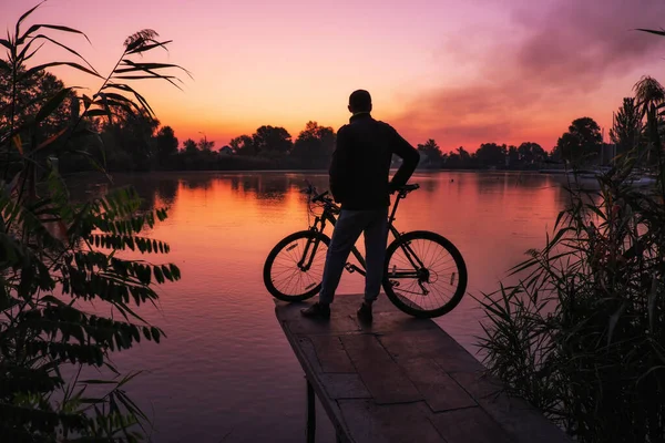 Człowiek z rowerem na czatach podziwia wschód lub zachód słońca.. — Zdjęcie stockowe