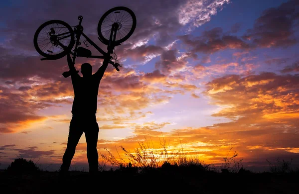 Silhouette the man stand in action lifting bicycle above his hea — Stock Photo, Image