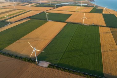 Yenilenebilir yel değirmenlerinin hava görüntüsü, ekolojik enerji sağlayan türbinler. Denizin yanındaki geniş tarım çayırlarında esen rüzgardan enerji alıyorlar. Alternatif elektrik