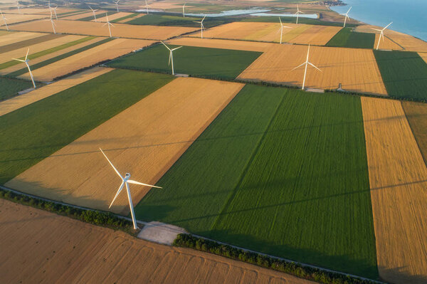 Aerial view of renewable windmills turbines supplying cultivation area with eco power getting energy from wind blowing on vast area of agriculture meadows next to sea. Alternative electricity