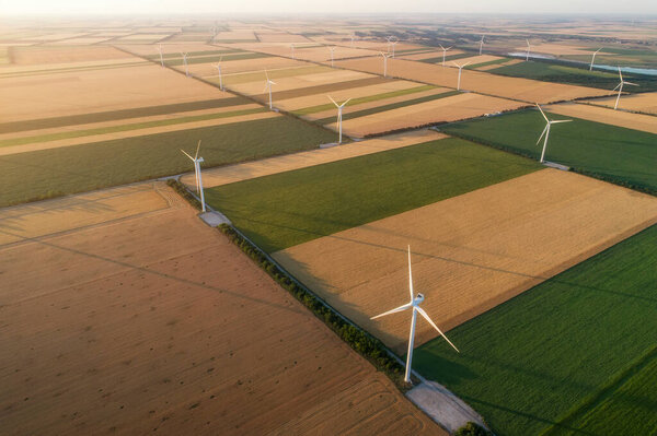 Aerial view of renewable windmills turbines supplying cultivation area with eco power getting energy from wind blowing on vast area of agriculture meadows next to sea. Alternative electricity