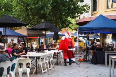 Gold Coast, Queensland, Avustralya - Aralık, 2018: Omzunda kırmızı bir çanta ile Noel Baba Zümrüt Göller pazarı yakınındaki sokakta kafede oturan insanlar geçen.